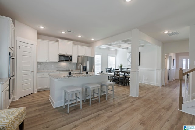 kitchen featuring stainless steel appliances, light hardwood / wood-style flooring, and a center island with sink