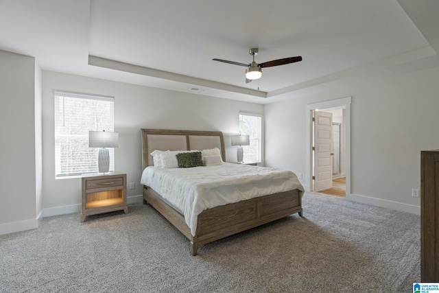 carpeted bedroom featuring a tray ceiling, ceiling fan, and ensuite bathroom