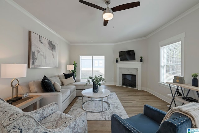 living room featuring light hardwood / wood-style flooring, ceiling fan, crown molding, and a premium fireplace