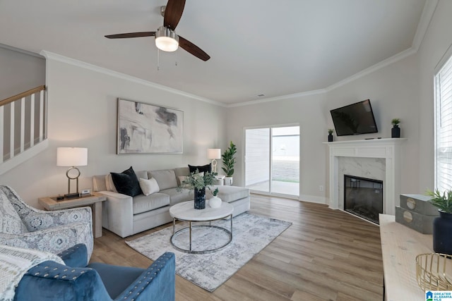 living room featuring light wood-type flooring, ceiling fan, crown molding, and a premium fireplace