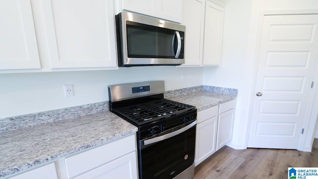 kitchen with light stone countertops, stainless steel appliances, white cabinetry, and light hardwood / wood-style floors