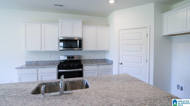 kitchen with white cabinets, appliances with stainless steel finishes, light stone countertops, and sink