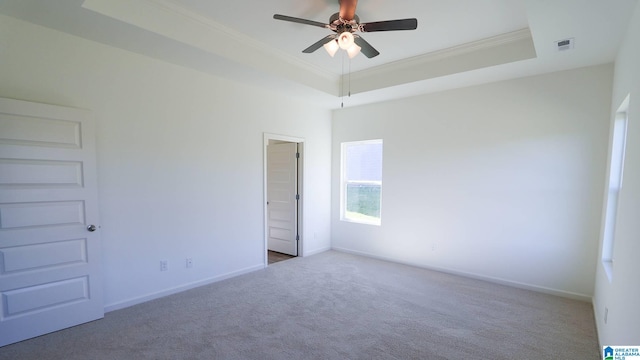 carpeted empty room featuring a raised ceiling, crown molding, and ceiling fan