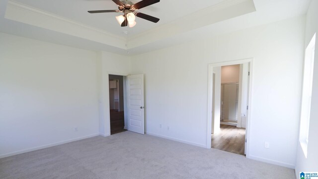 unfurnished bedroom with ceiling fan, a raised ceiling, ornamental molding, and light carpet