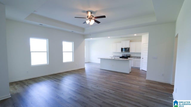 unfurnished living room featuring dark hardwood / wood-style floors, ceiling fan, and a tray ceiling