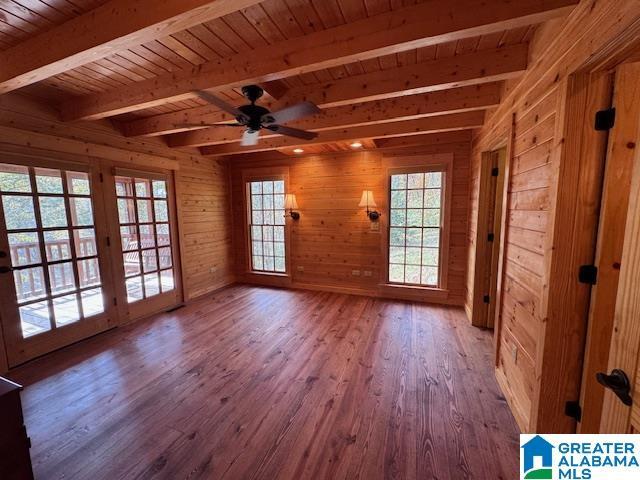 unfurnished room with ceiling fan, wooden ceiling, beamed ceiling, wood-type flooring, and wooden walls