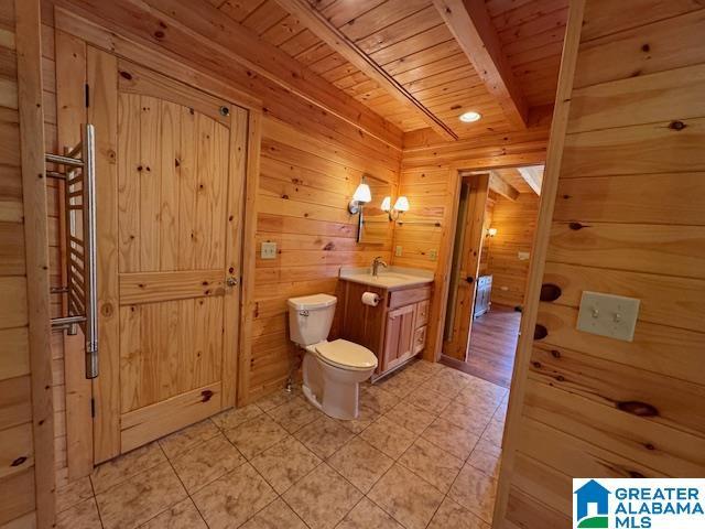 bathroom featuring beam ceiling, wood walls, wooden ceiling, and toilet