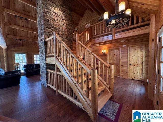 stairs with wooden walls, wood-type flooring, high vaulted ceiling, wooden ceiling, and beamed ceiling