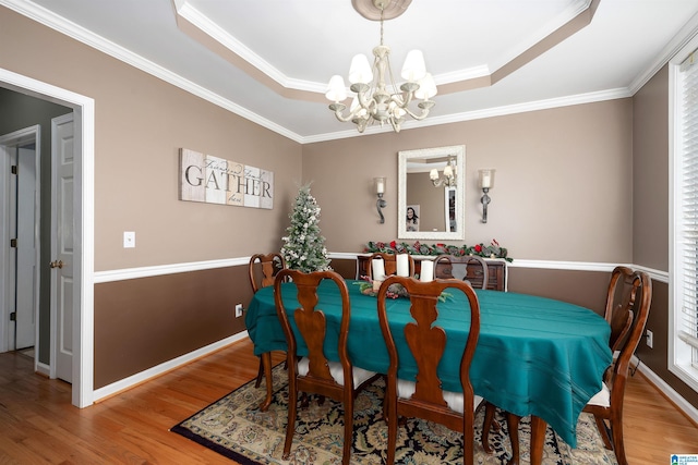 dining area with a raised ceiling, ornamental molding, light hardwood / wood-style flooring, and a chandelier