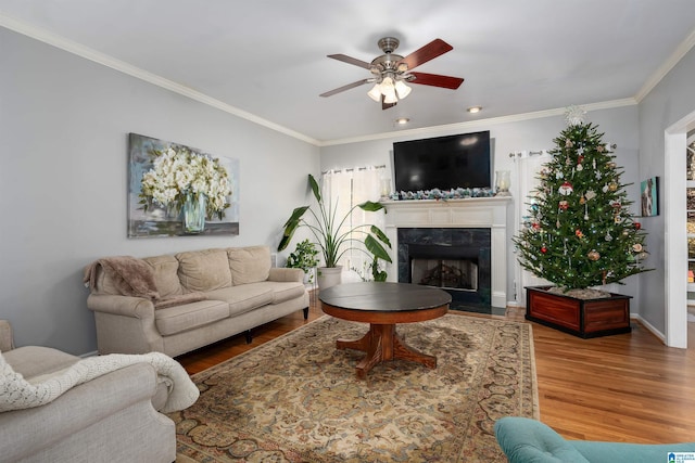 living room featuring hardwood / wood-style floors, ceiling fan, crown molding, and a high end fireplace