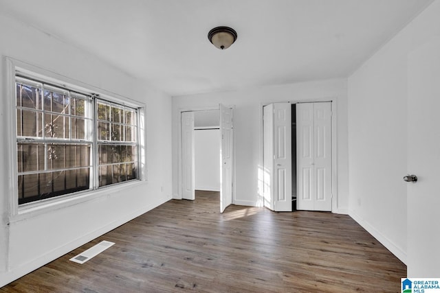 unfurnished bedroom with multiple closets and dark wood-type flooring