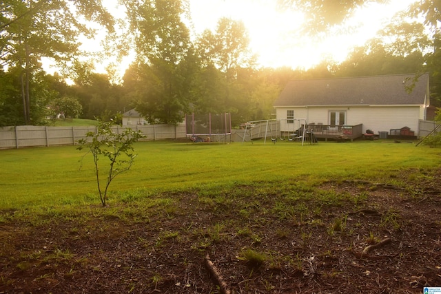 yard at dusk with a deck and a trampoline