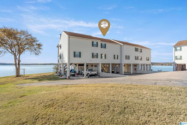 back of property with a lawn, a carport, and a water view