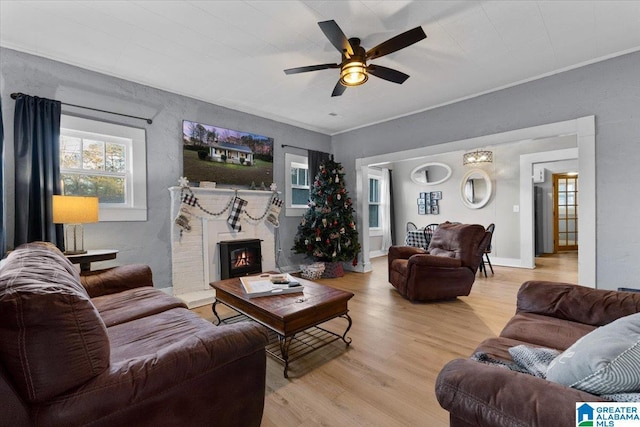 living room featuring a wood stove, light hardwood / wood-style flooring, ceiling fan, and ornamental molding