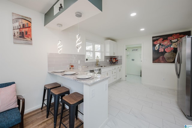 kitchen featuring white cabinetry, kitchen peninsula, stainless steel fridge, pendant lighting, and a breakfast bar