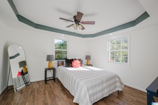 bedroom with hardwood / wood-style flooring, ceiling fan, and a tray ceiling