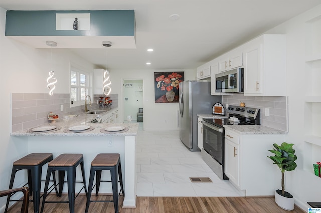 kitchen with white cabinets, light stone countertops, light hardwood / wood-style floors, kitchen peninsula, and stainless steel appliances