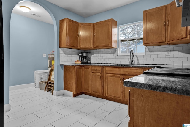 kitchen featuring decorative backsplash, sink, dark stone counters, and stovetop