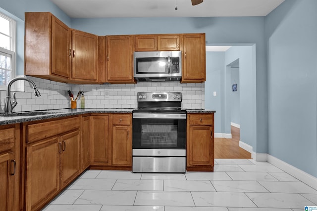 kitchen featuring backsplash, dark stone counters, sink, ceiling fan, and stainless steel appliances