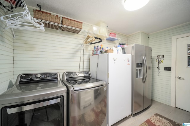 clothes washing area featuring washer and dryer, a textured ceiling, and wood walls