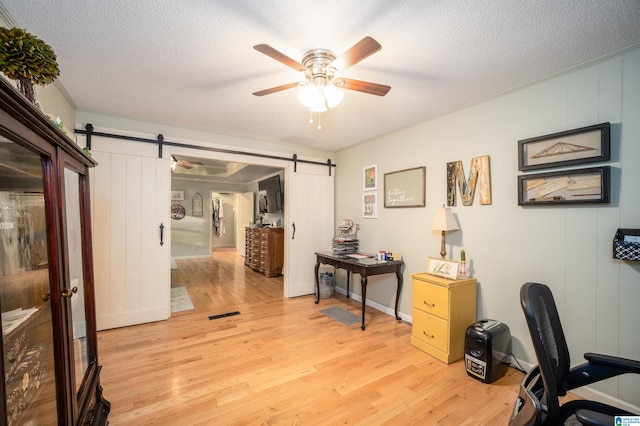 office space with a textured ceiling, a barn door, light hardwood / wood-style flooring, and ceiling fan