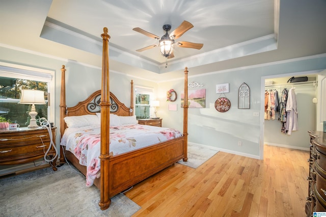 bedroom featuring ceiling fan, a spacious closet, a tray ceiling, light hardwood / wood-style floors, and a closet