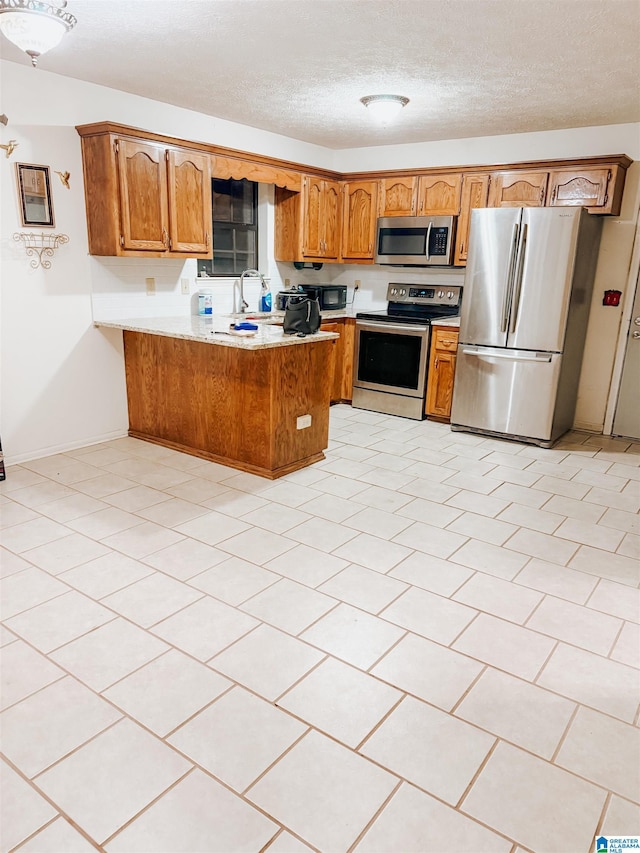 kitchen featuring kitchen peninsula, light tile patterned floors, a textured ceiling, and stainless steel appliances