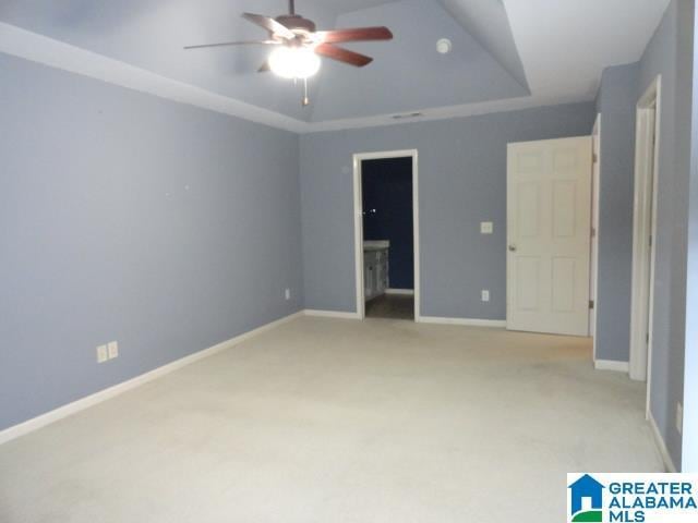 unfurnished bedroom featuring a raised ceiling, ceiling fan, light colored carpet, and ensuite bath