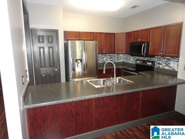 kitchen with sink, decorative backsplash, appliances with stainless steel finishes, dark hardwood / wood-style flooring, and kitchen peninsula