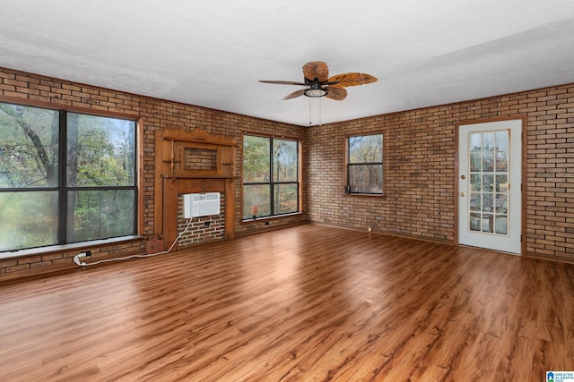 unfurnished living room with a wall mounted AC, light hardwood / wood-style flooring, ceiling fan, and brick wall