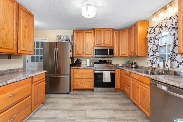 kitchen with sink, light wood-type flooring, a textured ceiling, and appliances with stainless steel finishes