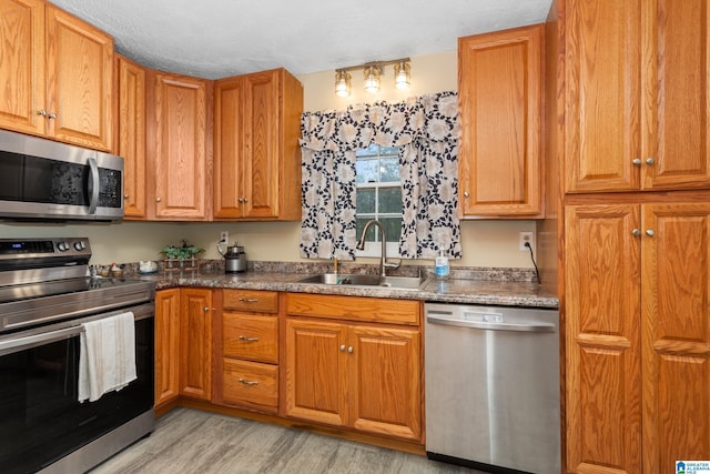 kitchen featuring a textured ceiling, sink, stainless steel appliances, and light hardwood / wood-style flooring