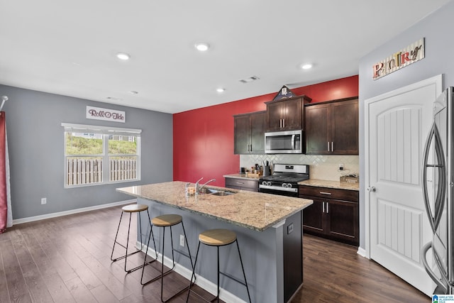 kitchen with sink, dark hardwood / wood-style floors, a breakfast bar area, a center island with sink, and appliances with stainless steel finishes