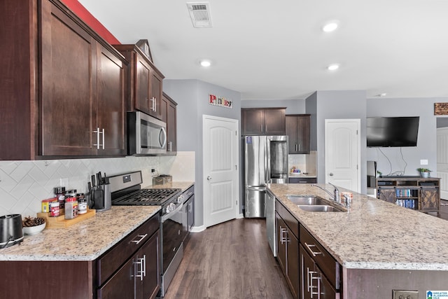 kitchen with sink, dark wood-type flooring, dark brown cabinets, a center island with sink, and appliances with stainless steel finishes