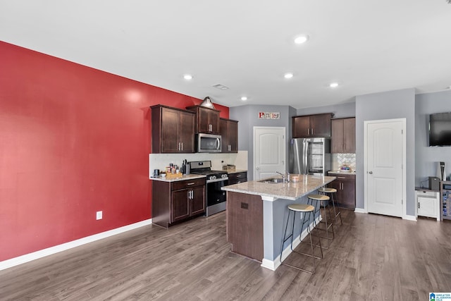 kitchen with sink, light stone counters, dark hardwood / wood-style flooring, an island with sink, and appliances with stainless steel finishes