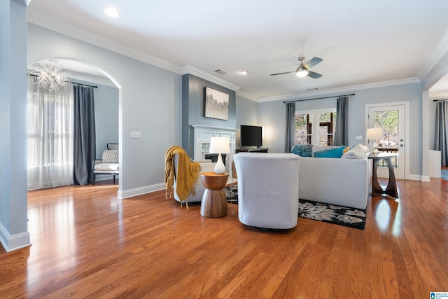 living room featuring wood-type flooring, ceiling fan with notable chandelier, and ornamental molding