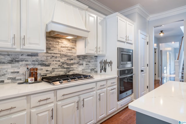 kitchen featuring backsplash, crown molding, custom range hood, white cabinetry, and stainless steel appliances