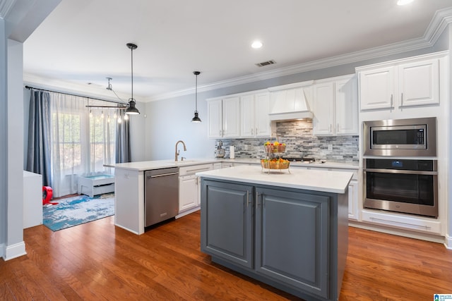 kitchen featuring pendant lighting, white cabinetry, custom range hood, and appliances with stainless steel finishes