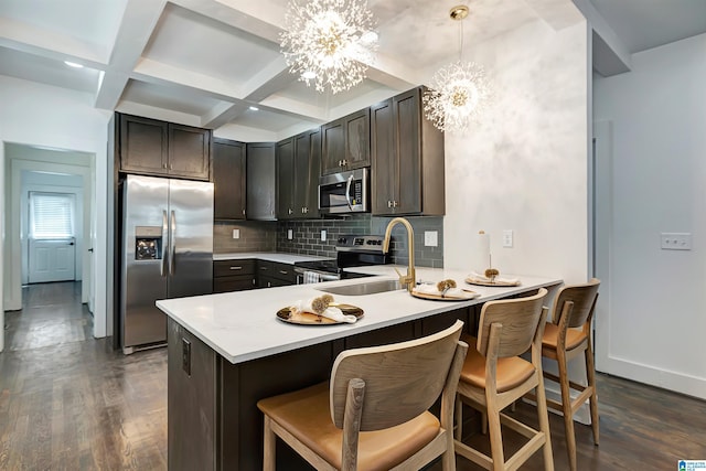 kitchen featuring coffered ceiling, stainless steel appliances, pendant lighting, an inviting chandelier, and dark hardwood / wood-style floors