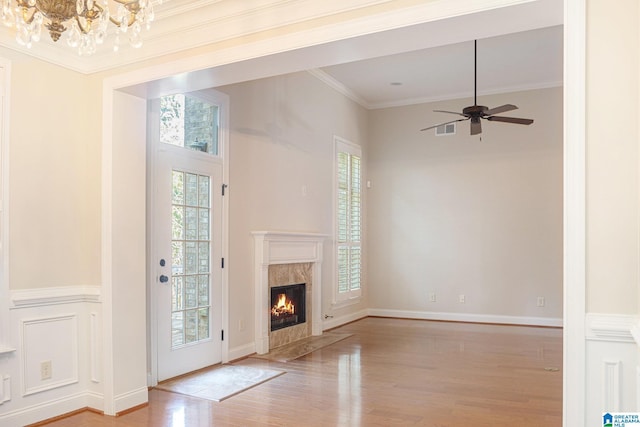 unfurnished living room with ceiling fan with notable chandelier, light hardwood / wood-style flooring, crown molding, and a premium fireplace