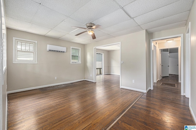 empty room with dark hardwood / wood-style flooring, a drop ceiling, ceiling fan, and a wall unit AC