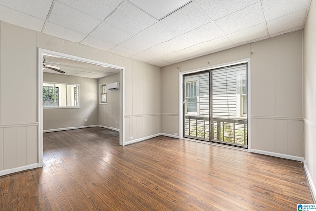 unfurnished room with an AC wall unit, a paneled ceiling, ceiling fan, and dark wood-type flooring