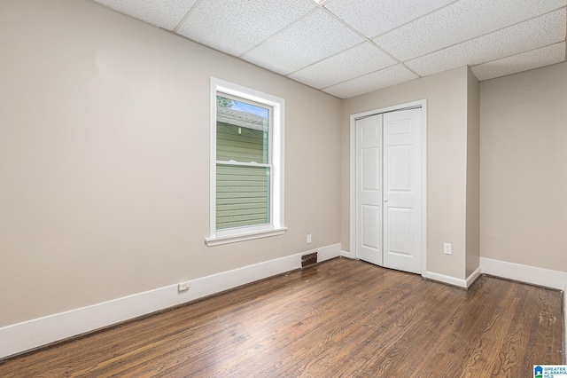 unfurnished bedroom featuring a drop ceiling, dark hardwood / wood-style flooring, and a closet