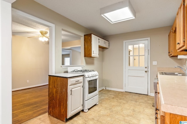 kitchen with sink, white gas range oven, light hardwood / wood-style flooring, ceiling fan, and a textured ceiling