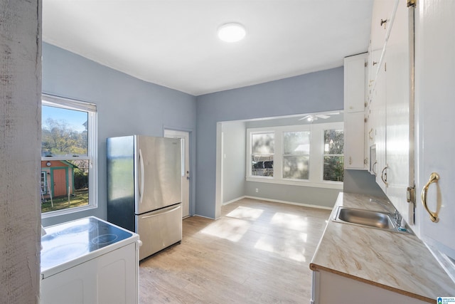 kitchen with white cabinets, sink, stainless steel fridge, light hardwood / wood-style floors, and range