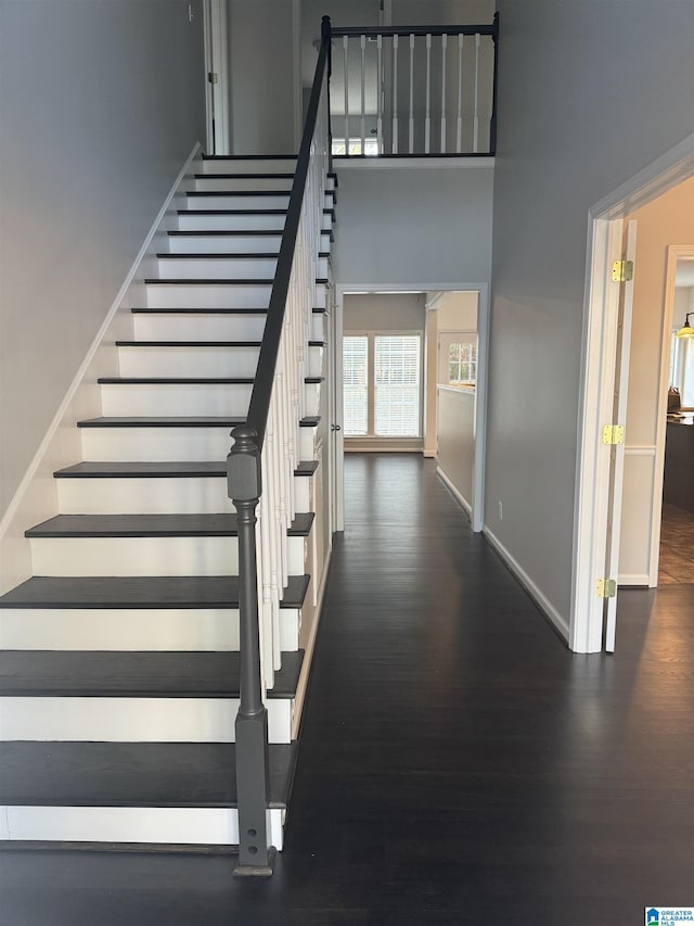 stairway with wood-type flooring and a towering ceiling