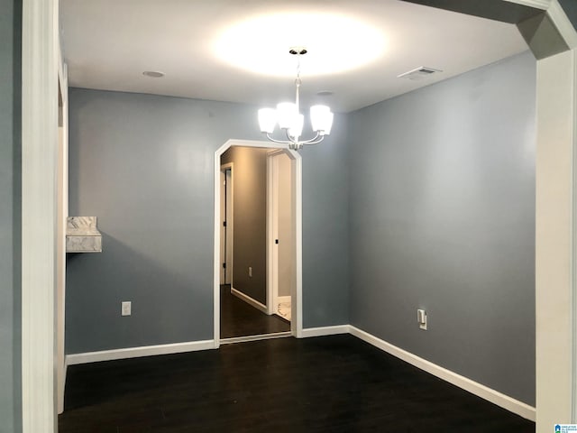 spare room featuring dark hardwood / wood-style flooring and a chandelier