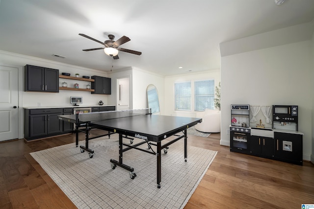 game room with ceiling fan, ornamental molding, and dark wood-type flooring