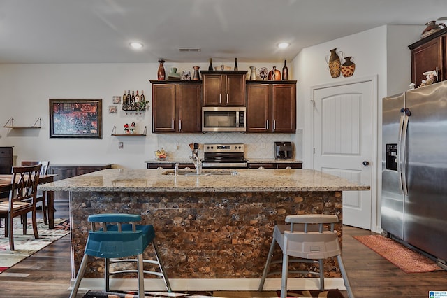 kitchen featuring sink, dark wood-type flooring, light stone counters, an island with sink, and appliances with stainless steel finishes