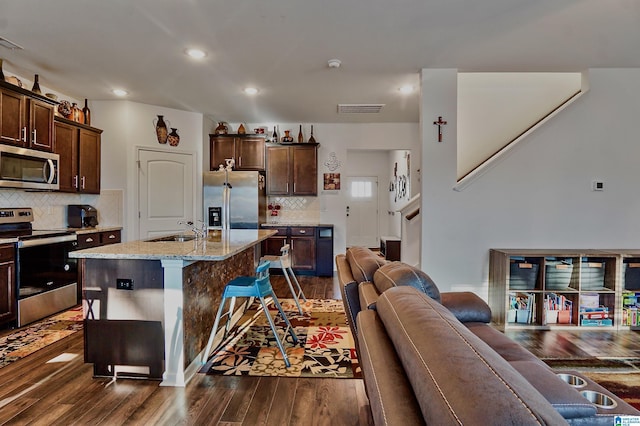 kitchen with a kitchen breakfast bar, dark hardwood / wood-style flooring, stainless steel appliances, sink, and an island with sink